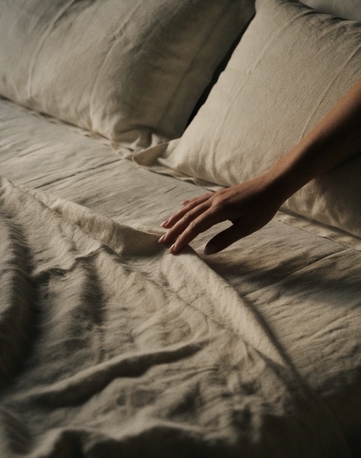A hand resting on washed linen sheets in low evening light