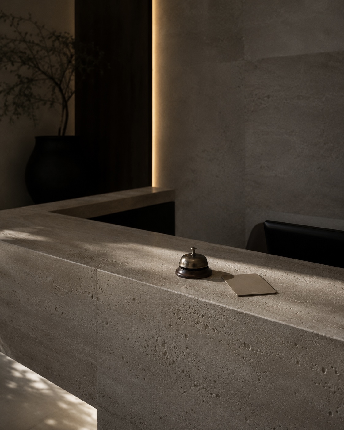 A travertine reception desk with a single brass bell, lit by a quiet arc of light