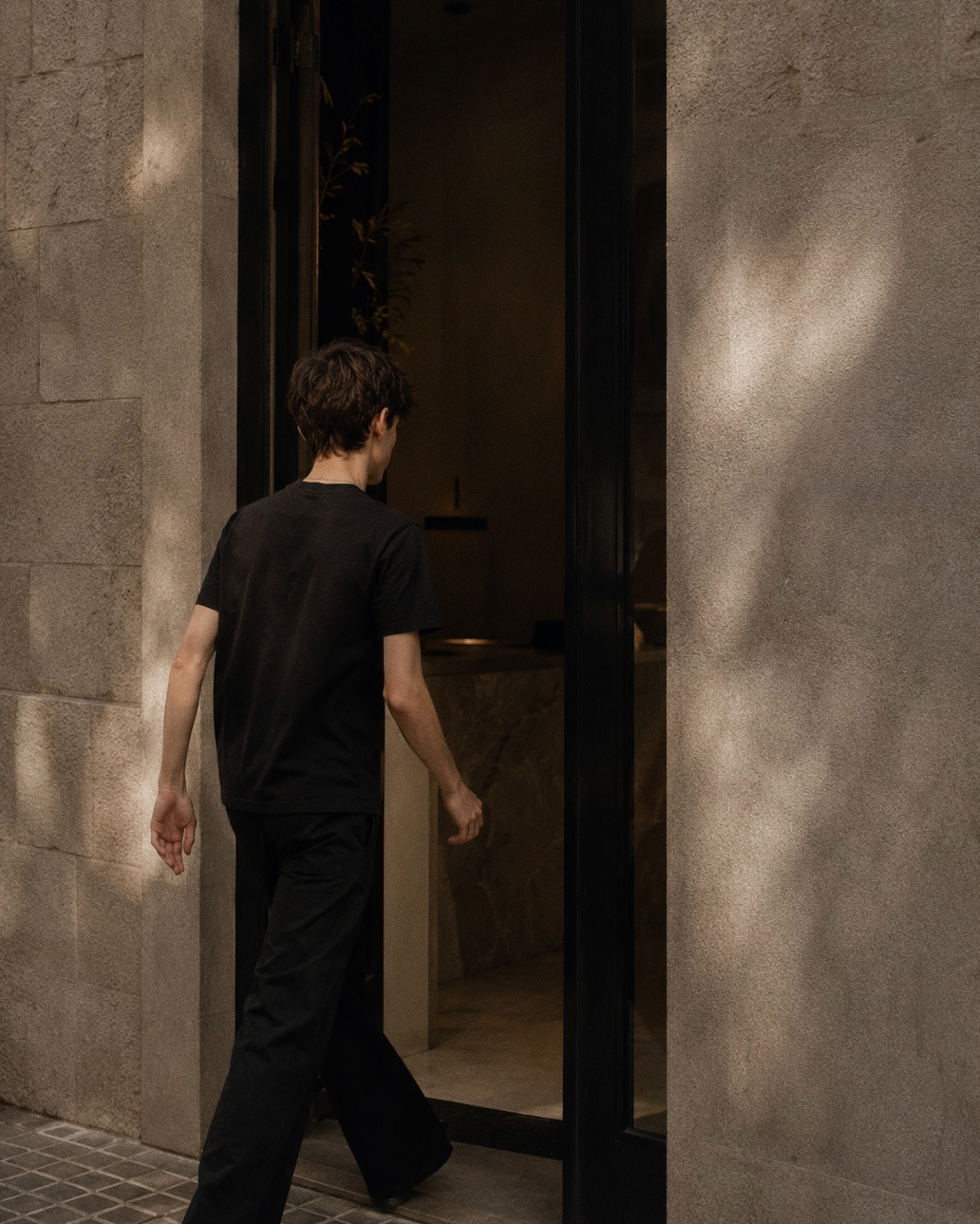 A figure stepping through a stone doorway into a quiet interior