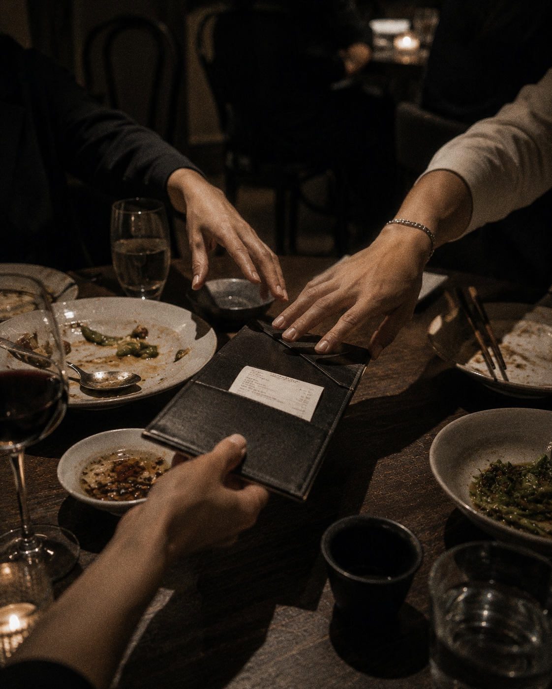 Several hands reaching for the bill at the end of a shared dinner