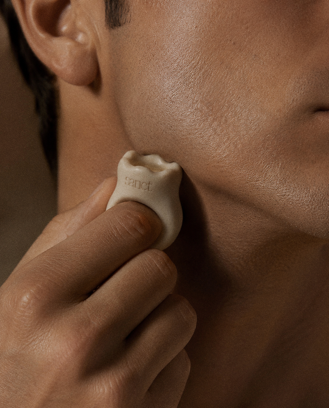 A hand-shaped Sanct ritual stone pressed gently to the jawline